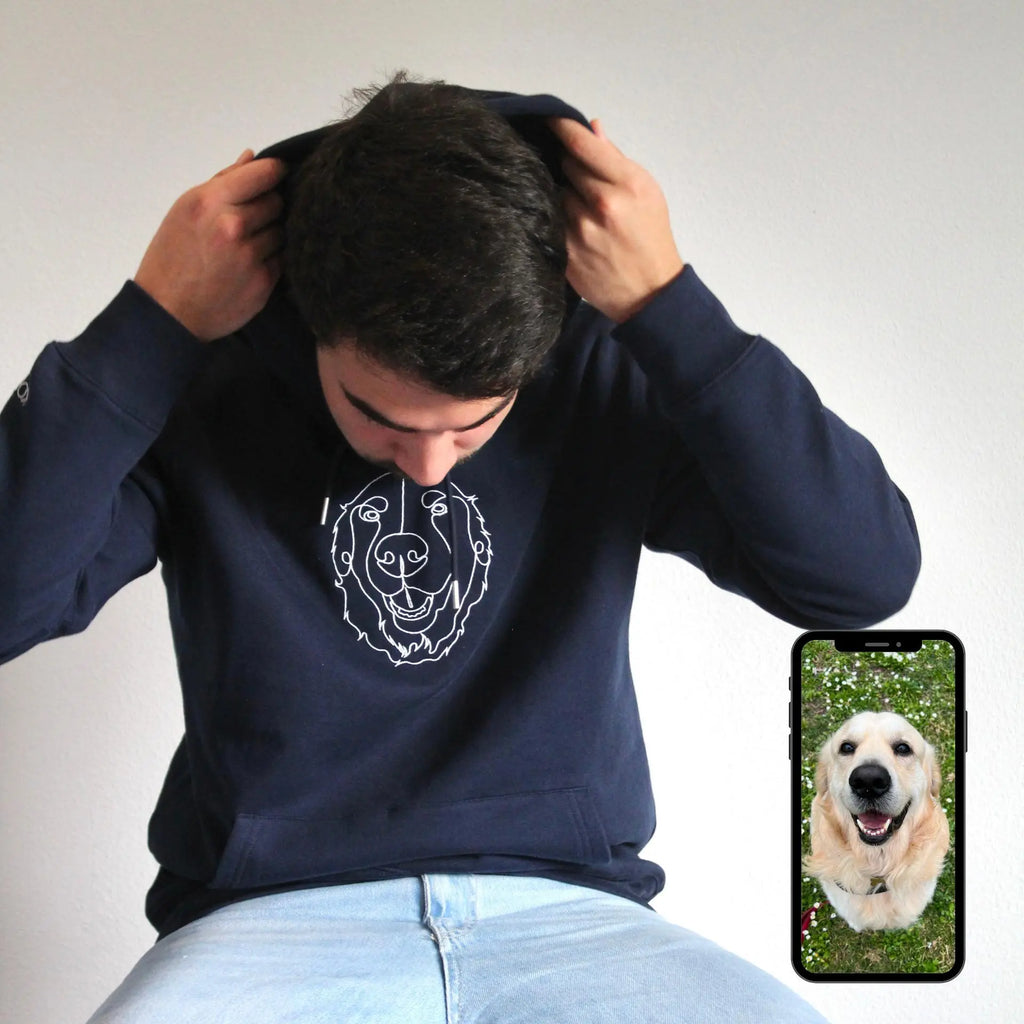Person wearing a navy blue sweatshirt with a bear graphic, holding their head with both hands, and a phone displaying a dog photo in the corner.