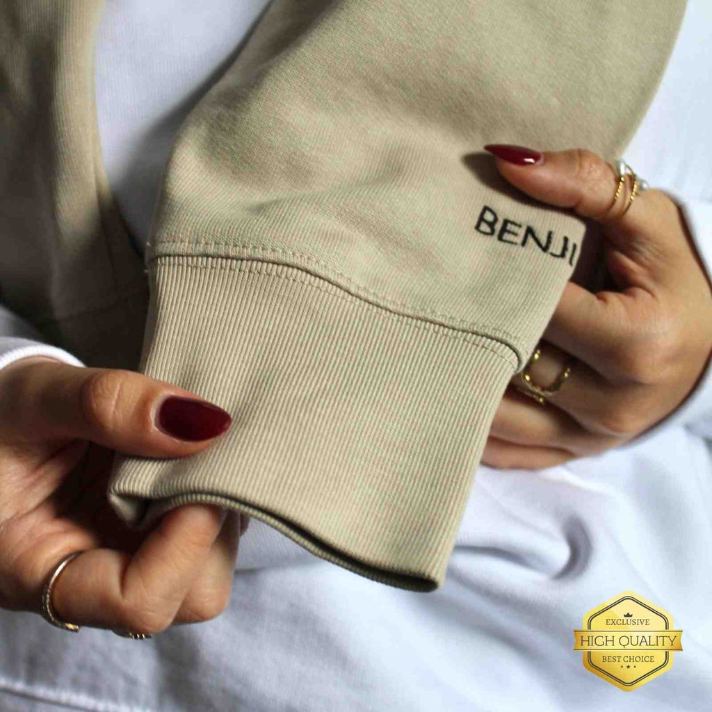 Beige sweatshirt with 'BENJI' branding held by hands against a white background