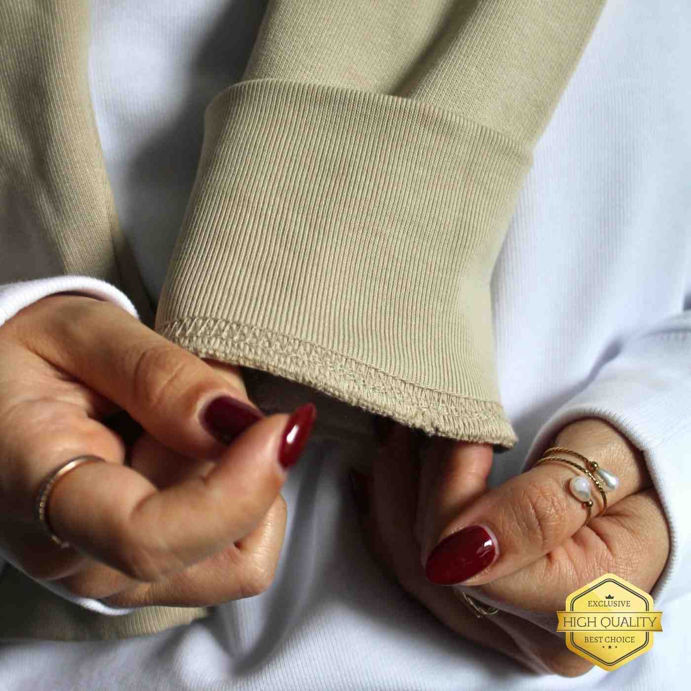 Close-up of hands wearing rings with a beige garment and white background