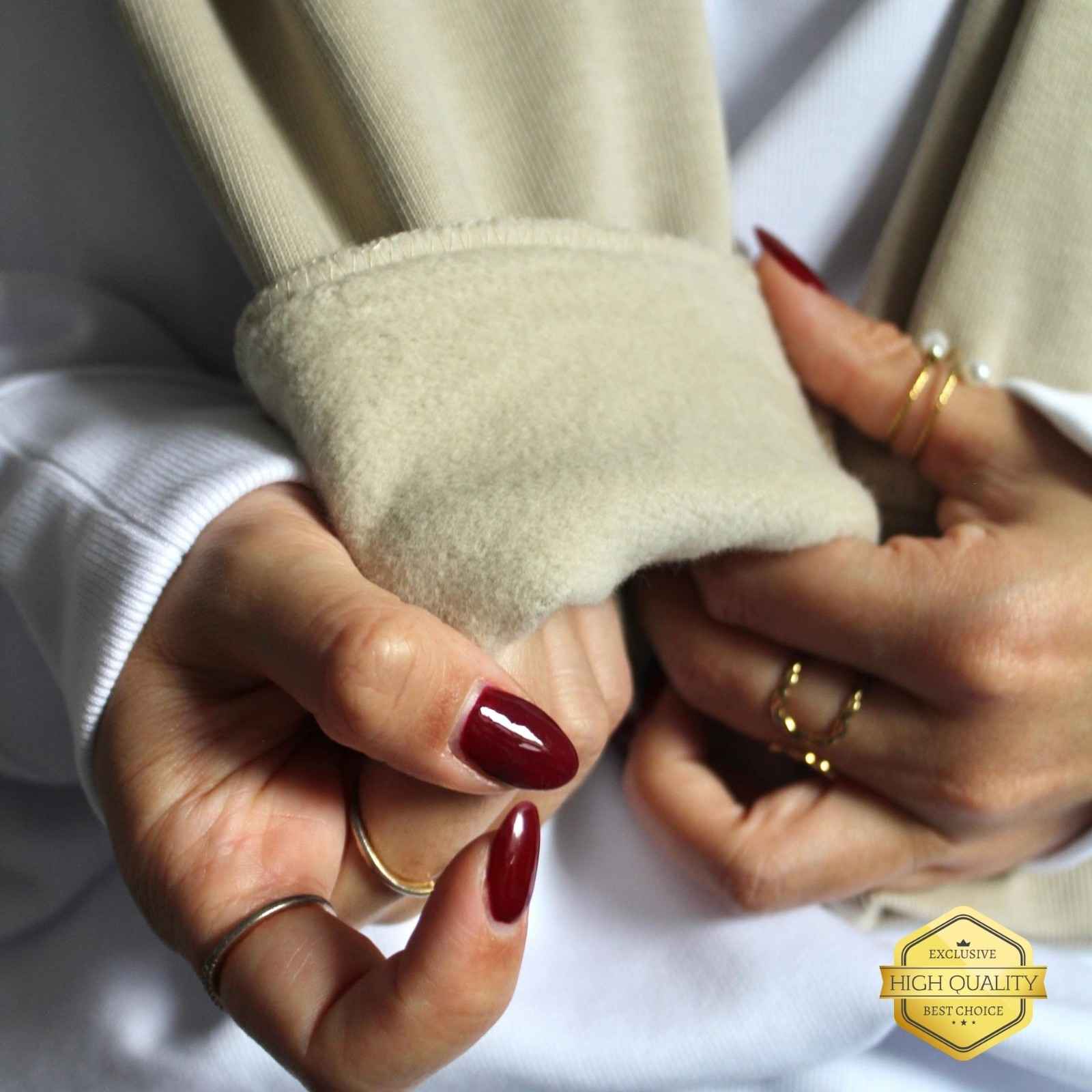 Close-up of hands with red nail polish wearing beige gloves and gold rings.