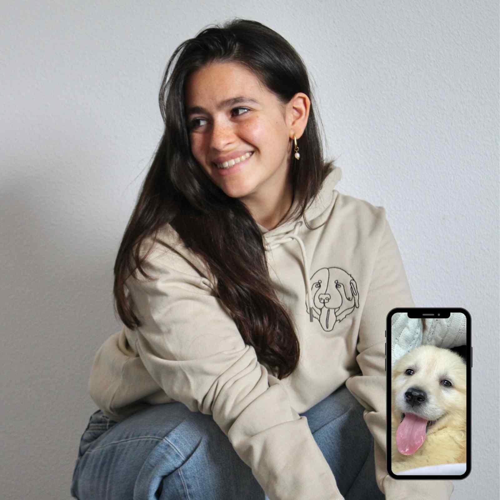 Woman wearing a beige hoodie with a dog graphic, holding a phone with a dog photo.
