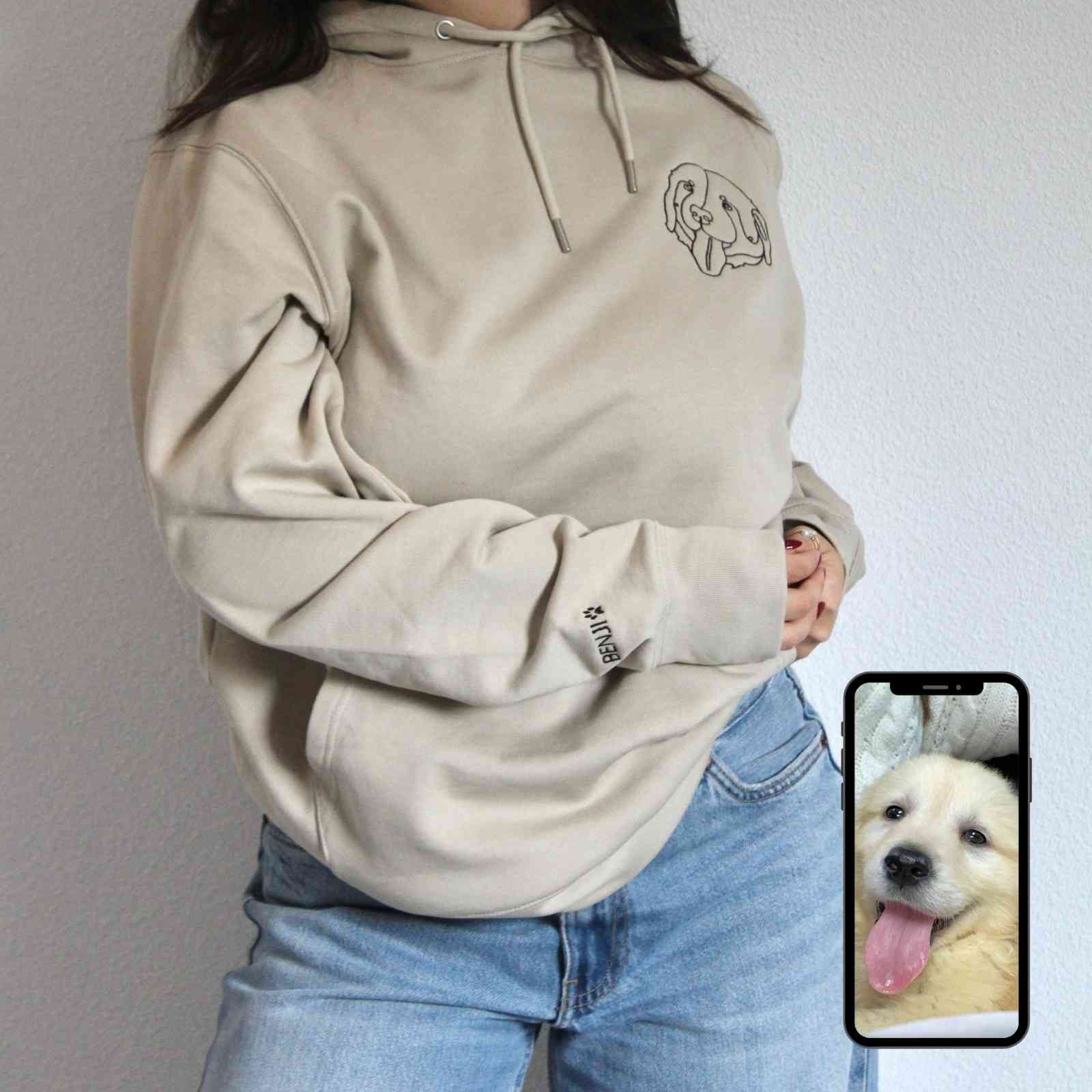 Person wearing a beige hoodie with a dog design, standing against a plain background.