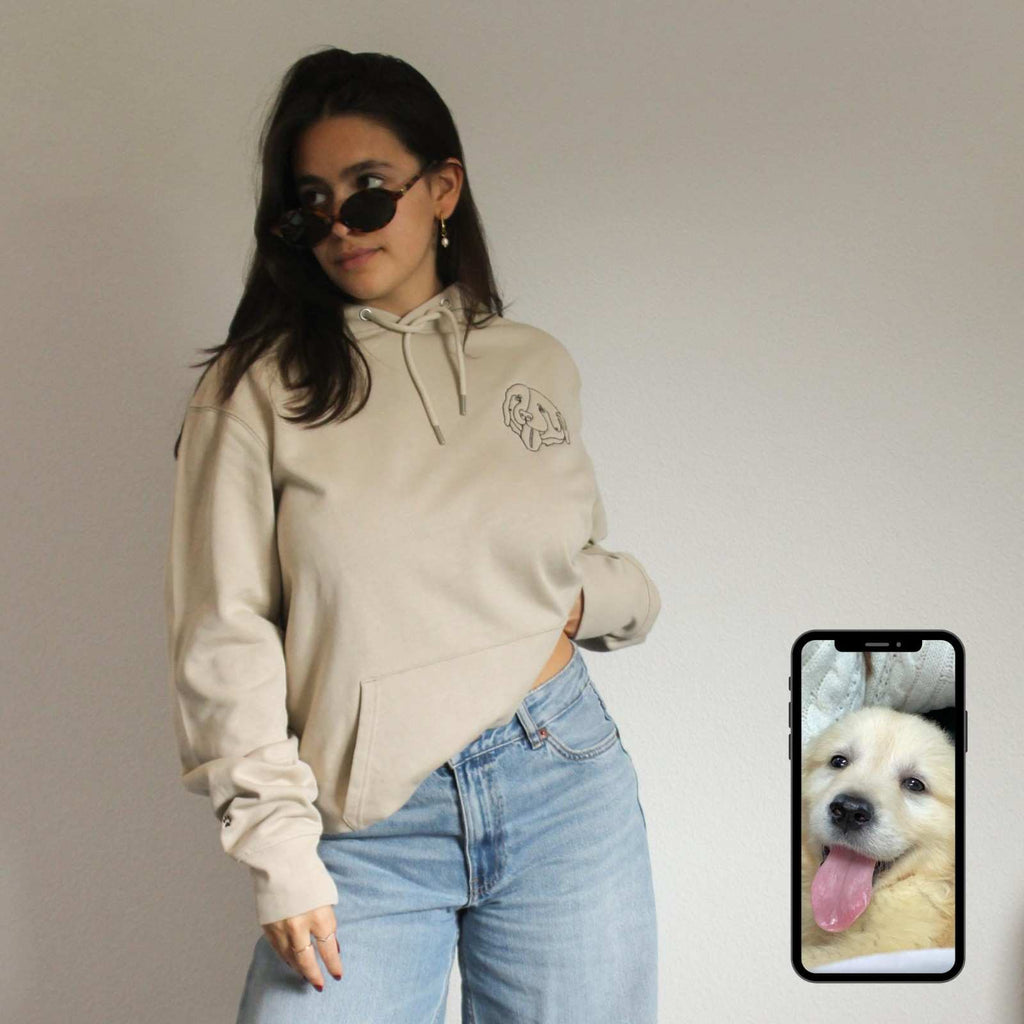 Woman wearing a beige hoodie and sunglasses with a phone displaying a dog's face.