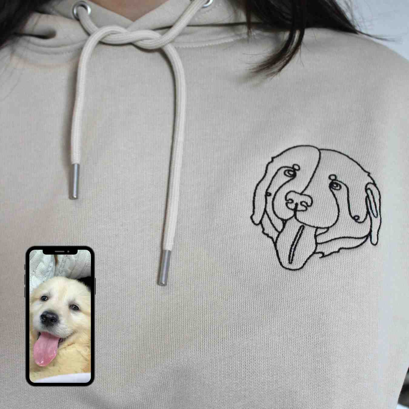 Light gray hoodie with a dog illustration on the chest, next to a smartphone displaying a photo of a puppy.