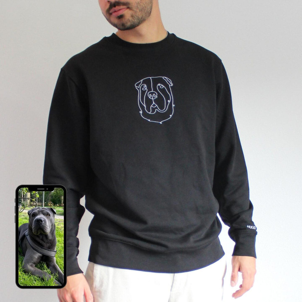 Person wearing a black sweatshirt with a dog design, holding a phone with a dog photo.