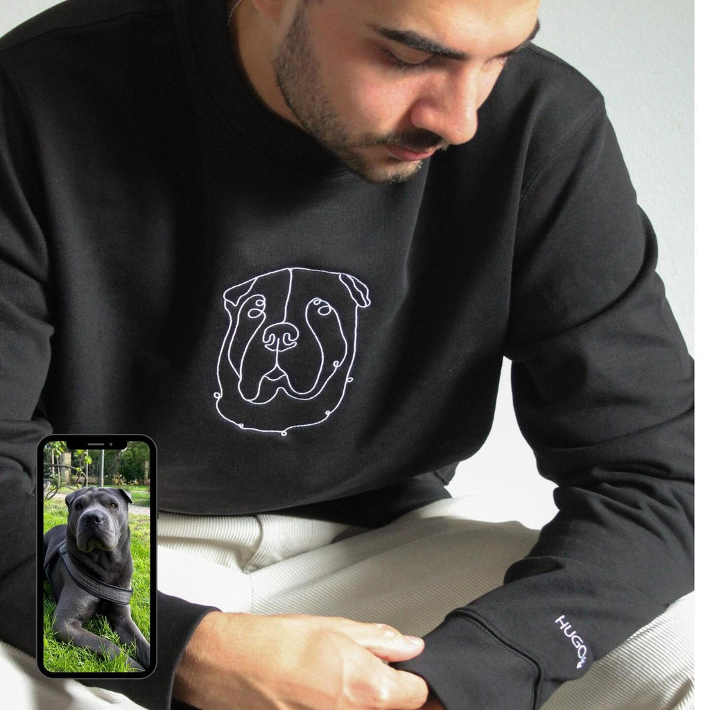 Man wearing a black sweatshirt with a bulldog design, holding a phone showing a photo of a dog.