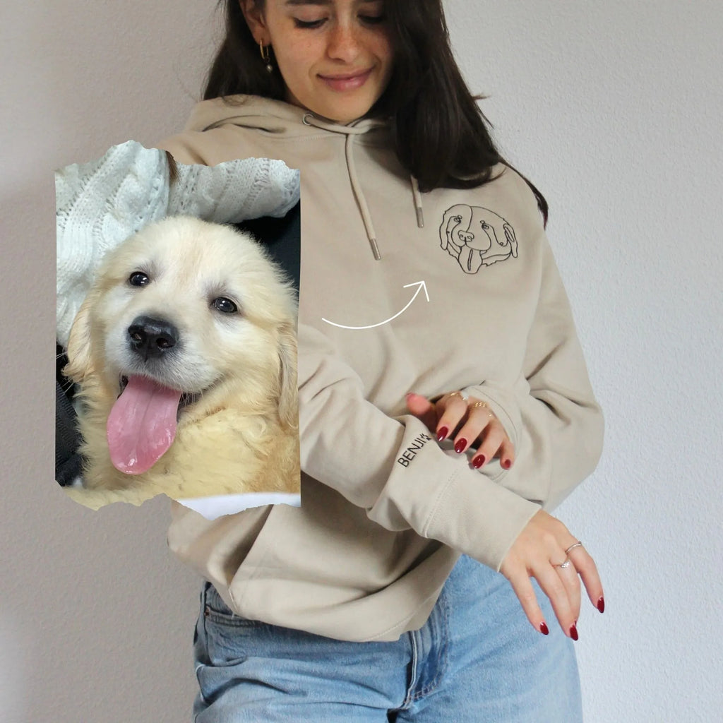 Person wearing a beige hoodie with a dog graphic, holding a photo of a dog.