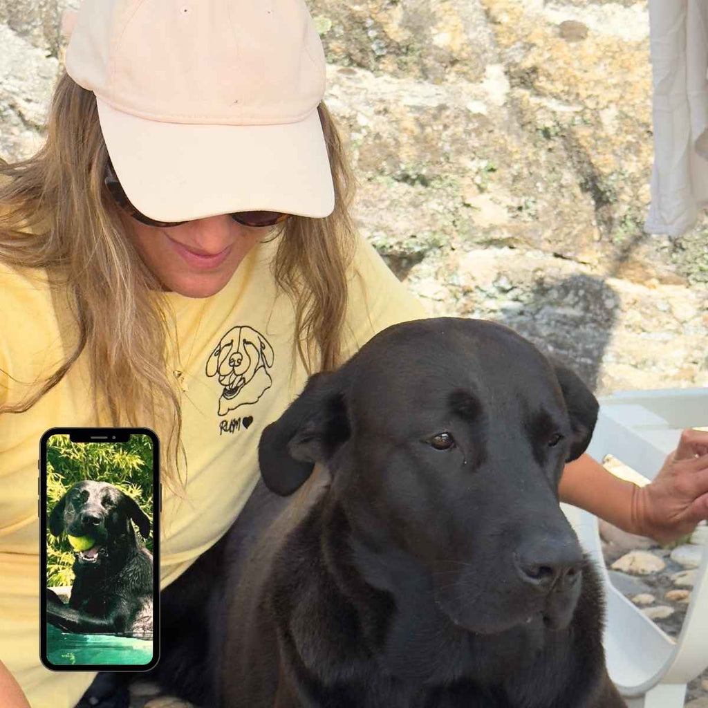 Person with a black dog outdoors, using a phone showing another dog on screen