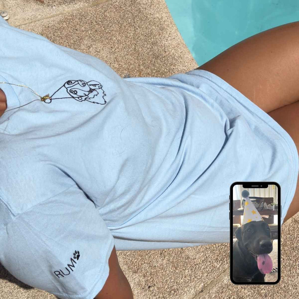 Person wearing a light blue shirt with a graphic design, sitting on sand next to a pool.