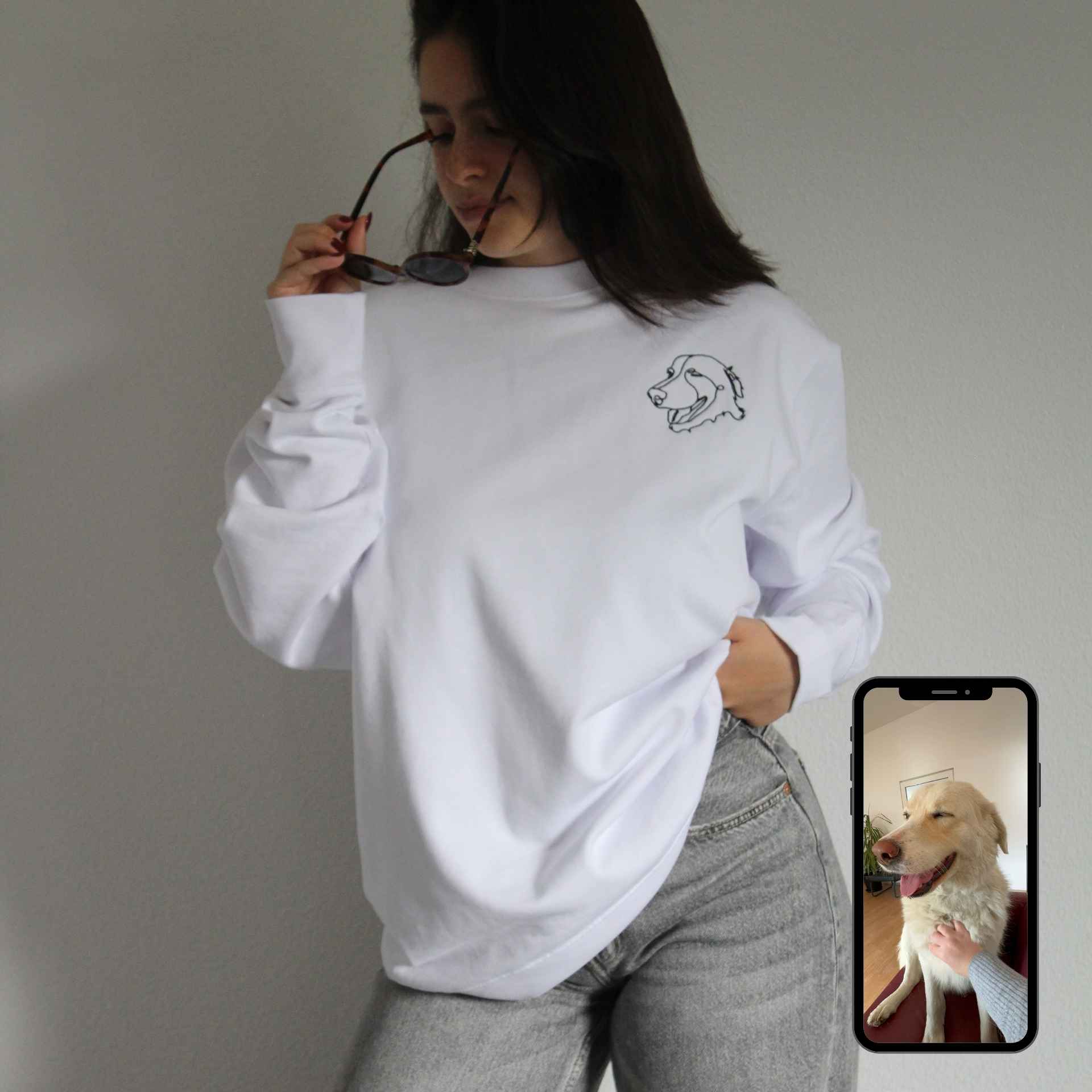 Person wearing a white sweatshirt with a dog design, holding sunglasses, and looking at a phone showing a dog photo.