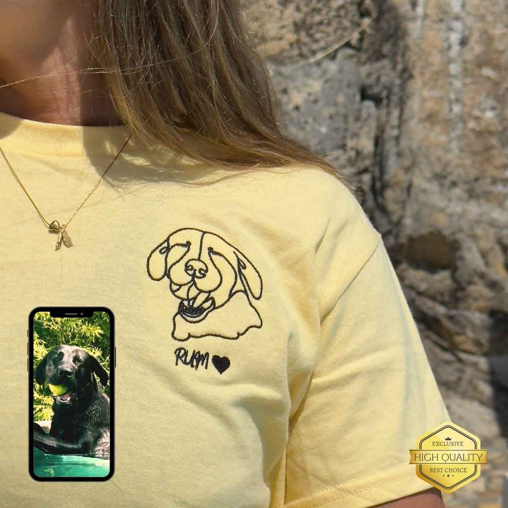 Person wearing a yellow shirt with a dog illustration and a phone displaying a photo of a dog.