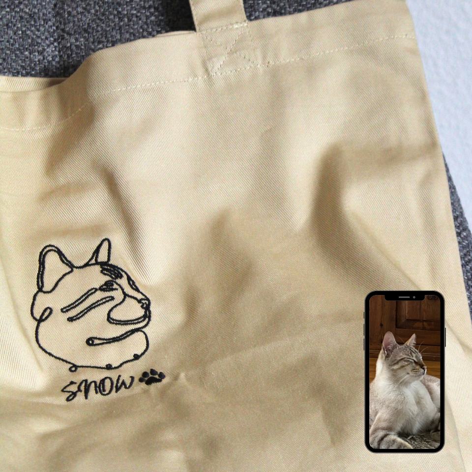 Beige tote bag with a dog illustration and 'Snow' text, next to a phone showing a cat.