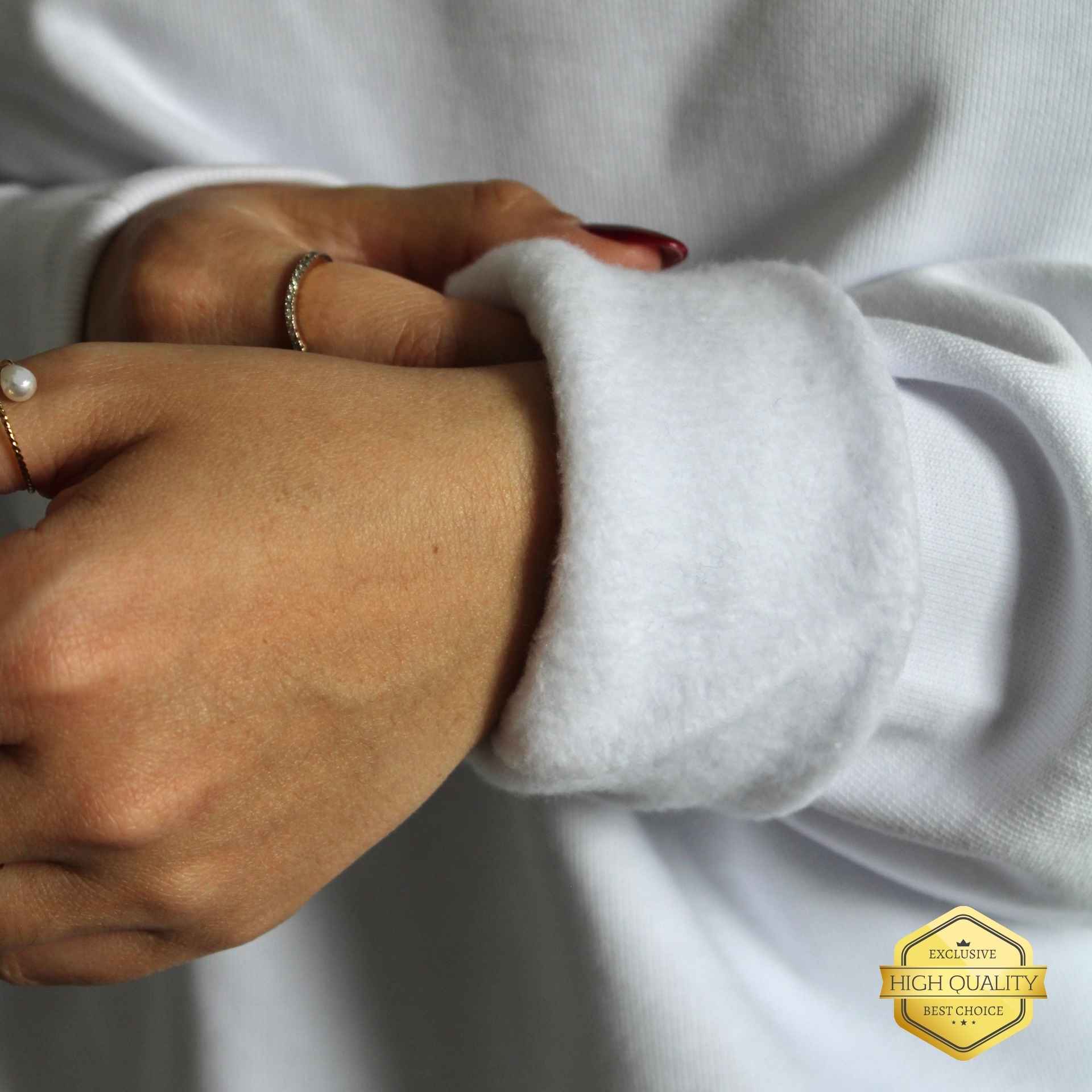 Close-up of a person's hands with a focus on jewelry, wearing a white sweater.
