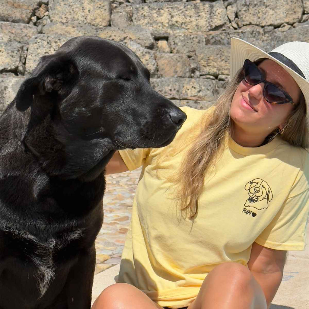Woman in a yellow shirt with a black dog sitting on stone steps.