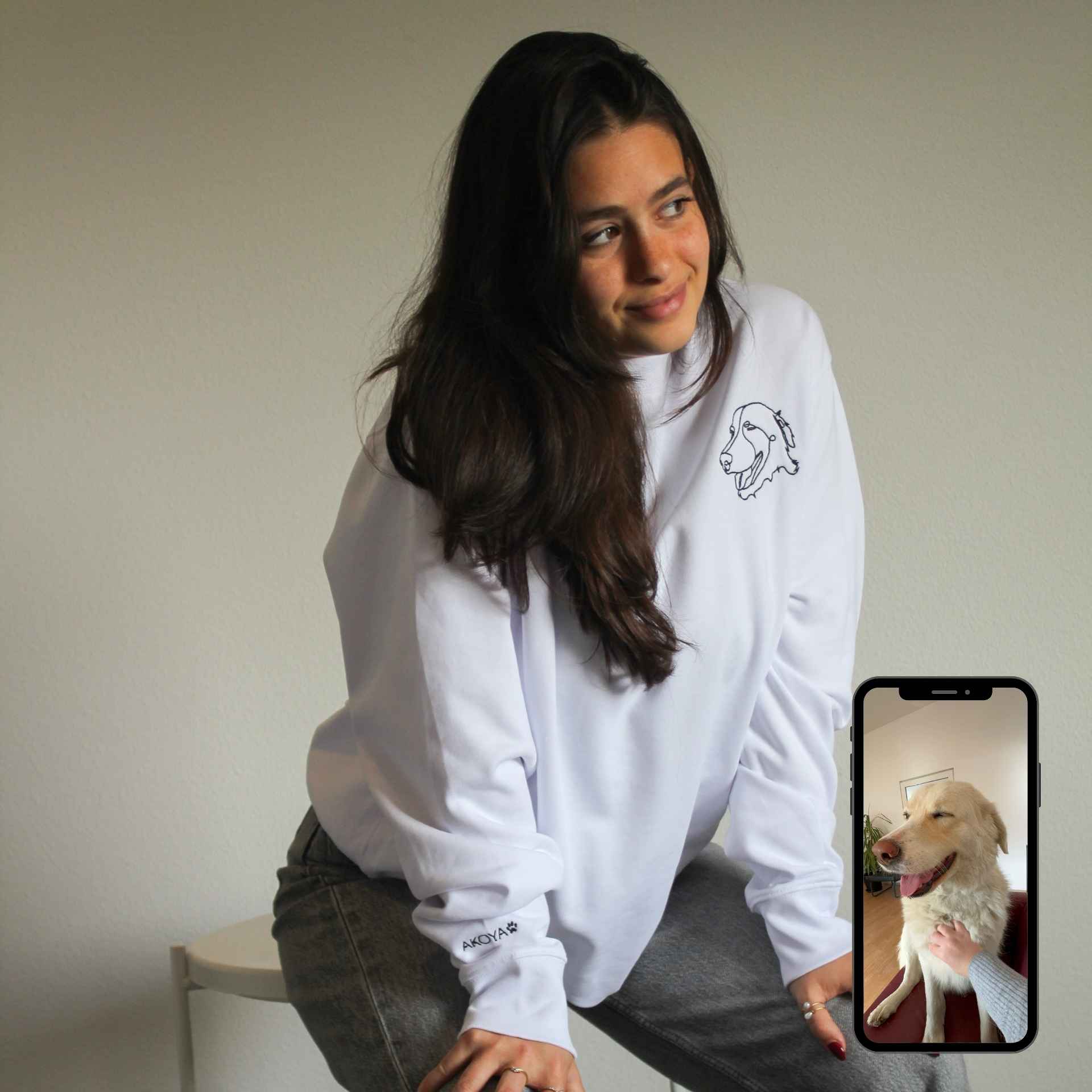 Woman wearing a white hoodie with a phone displaying a dog on a beige background