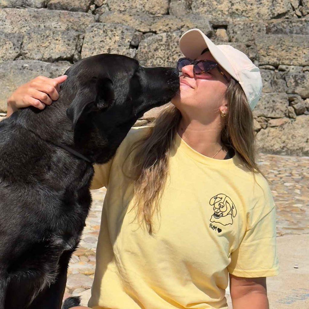 Woman in yellow shirt and cap with black dog outdoors