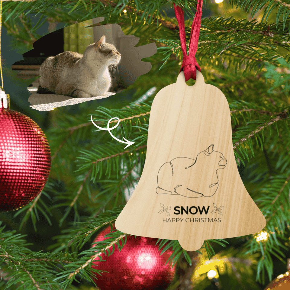 Wooden bell ornament with cat design and 'Snow Happy Christmas' text hanging on a Christmas tree.