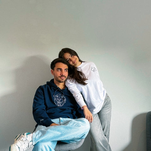 Two people sitting close together against a plain wall.