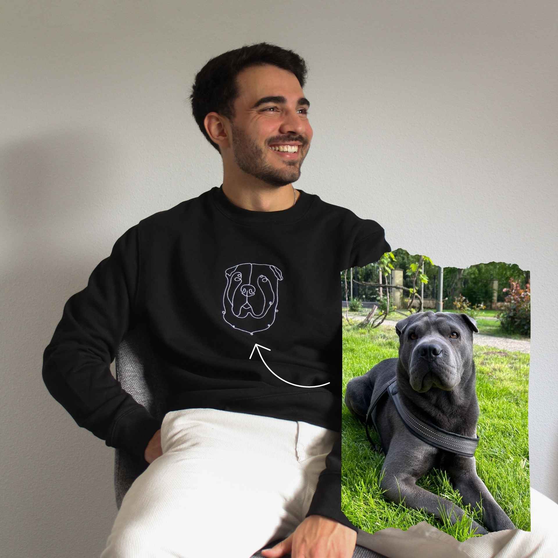 Man wearing a black sweatshirt with a dog design, sitting next to a photo of a dog on grass.