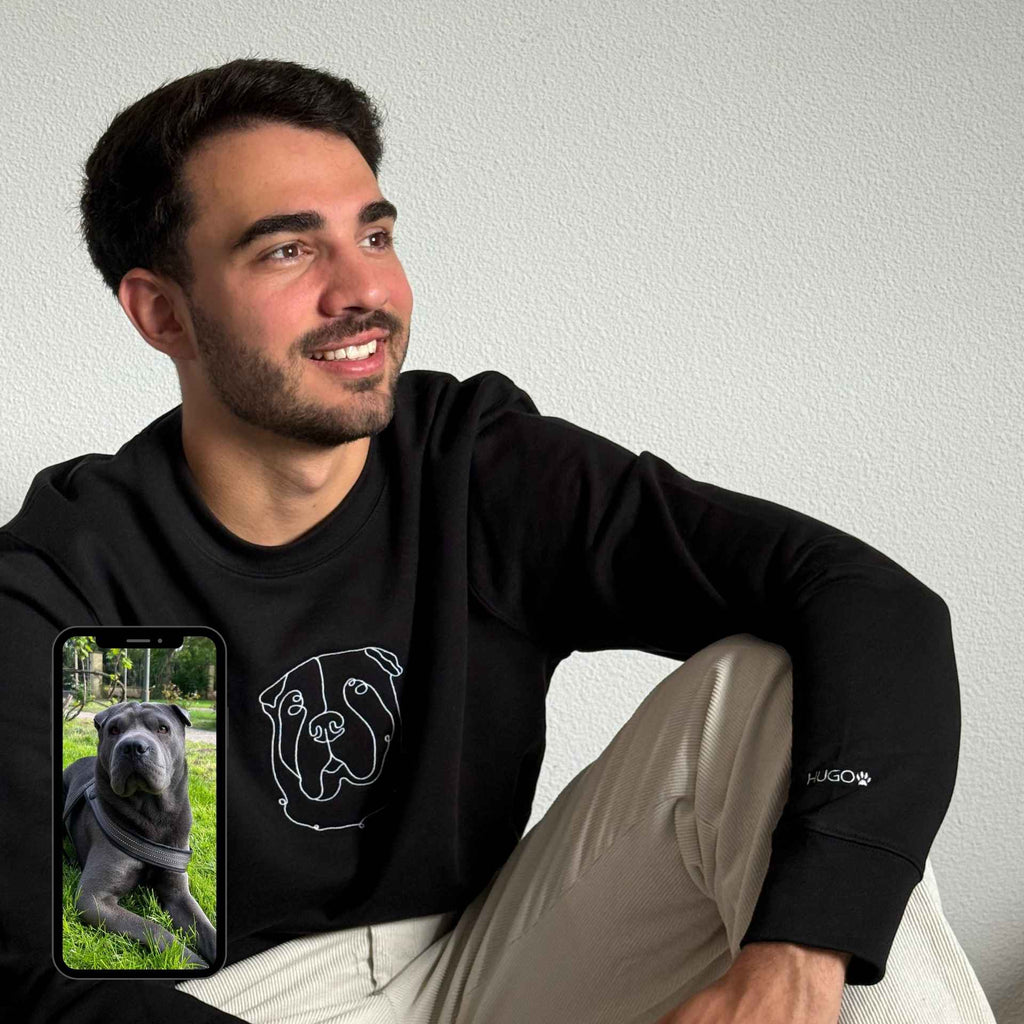 Man wearing a black hoodie with a dog graphic, sitting on a white couch.